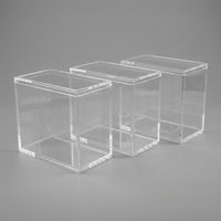 Three empty acrylic Elite Trainer Box display cases with lids on a neutral background